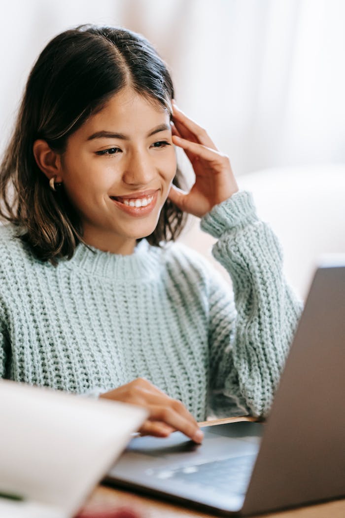 A young woman smiling as she uses a laptop in a cozy indoor setting, creating a comfortable workspace atmosphere.